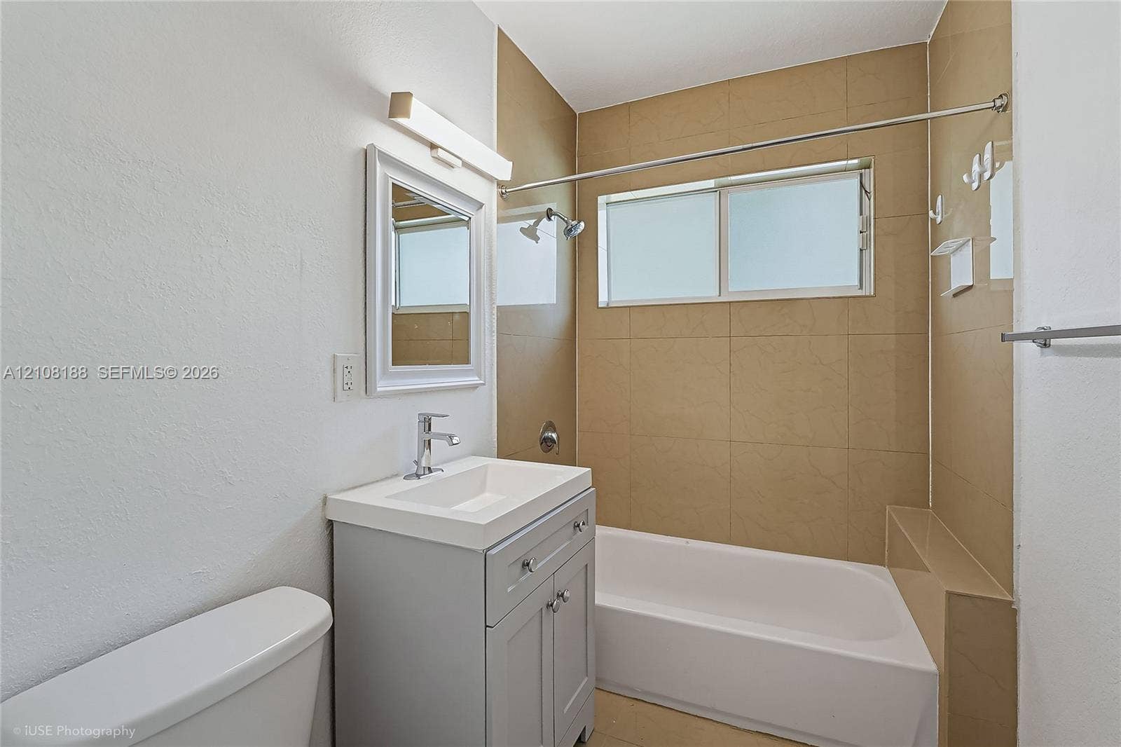 9790 E Bay Harbor Drive, #3N, Bay Harbor Islands, Bay Harbor Islands, FL 33154 Bathroom featuring a grey vanity with a rectangular sink, brushed nickel faucet, wall-mounted vanity light, and a tub-shower combination with floor-to-ceiling neutral tile surround