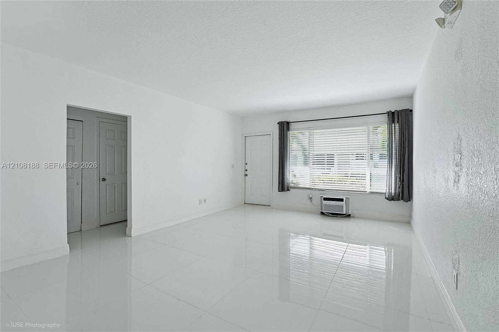 9790 E Bay Harbor Drive, #3N, Bay Harbor Islands, Bay Harbor Islands, FL 33154 Bright interior space featuring polished tile flooring, a large picture window with horizontal blinds, and a wall-mounted air conditioning unit