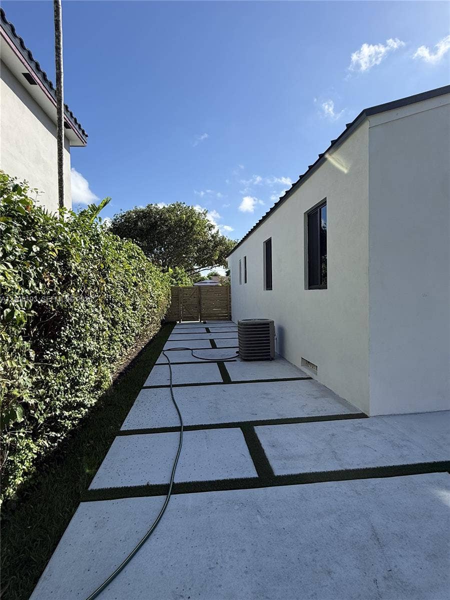 1929 SW 21st Street, #0, Miami, Miami, FL 33145 Exterior side yard featuring a concrete paver walkway with integrated turf lines, a mature hedgerow, and a wood-slat privacy screen