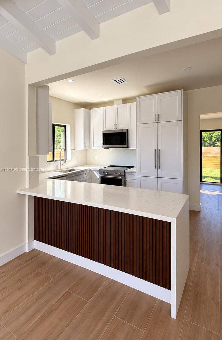 1929 SW 21st Street, #0, Miami, Miami, FL 33145 Kitchen featuring white cabinetry, wood-finish flooring, a waterfall edge countertop, a slatted wood-paneled island, and recessed ceiling beams
