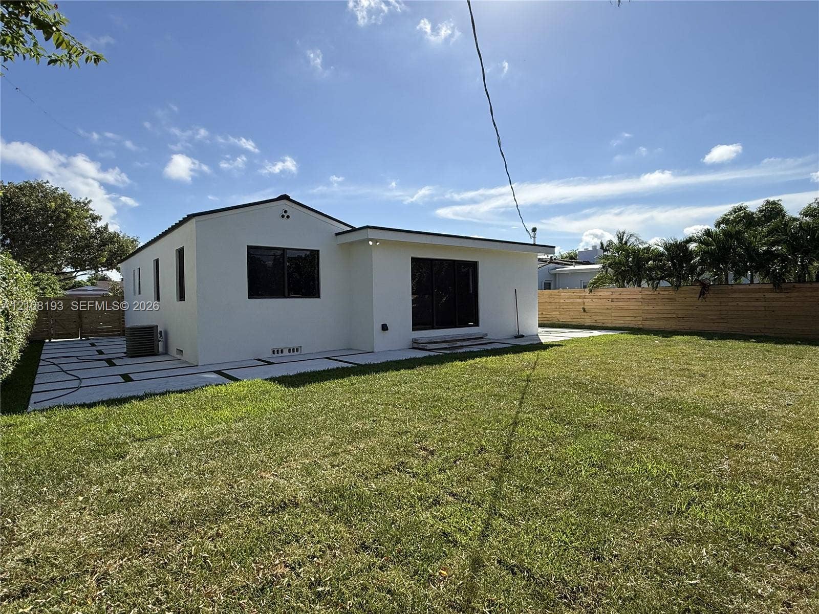 1929 SW 21st Street, #0, Miami, Miami, FL 33145 Stucco exterior with a low-pitch roof, expansive grass lawn, large geometric paver patio, and horizontal wood privacy fencing