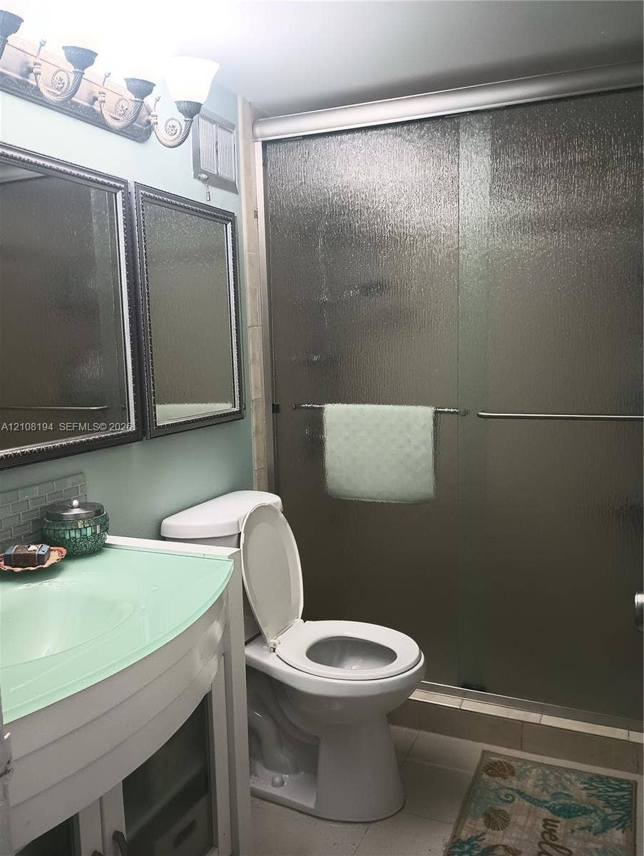Bathroom featuring a vanity with a translucent green countertop, dual framed wall-mounted mirrors, a multi-light fixture, and a walk-in shower with textured glass sliding doors