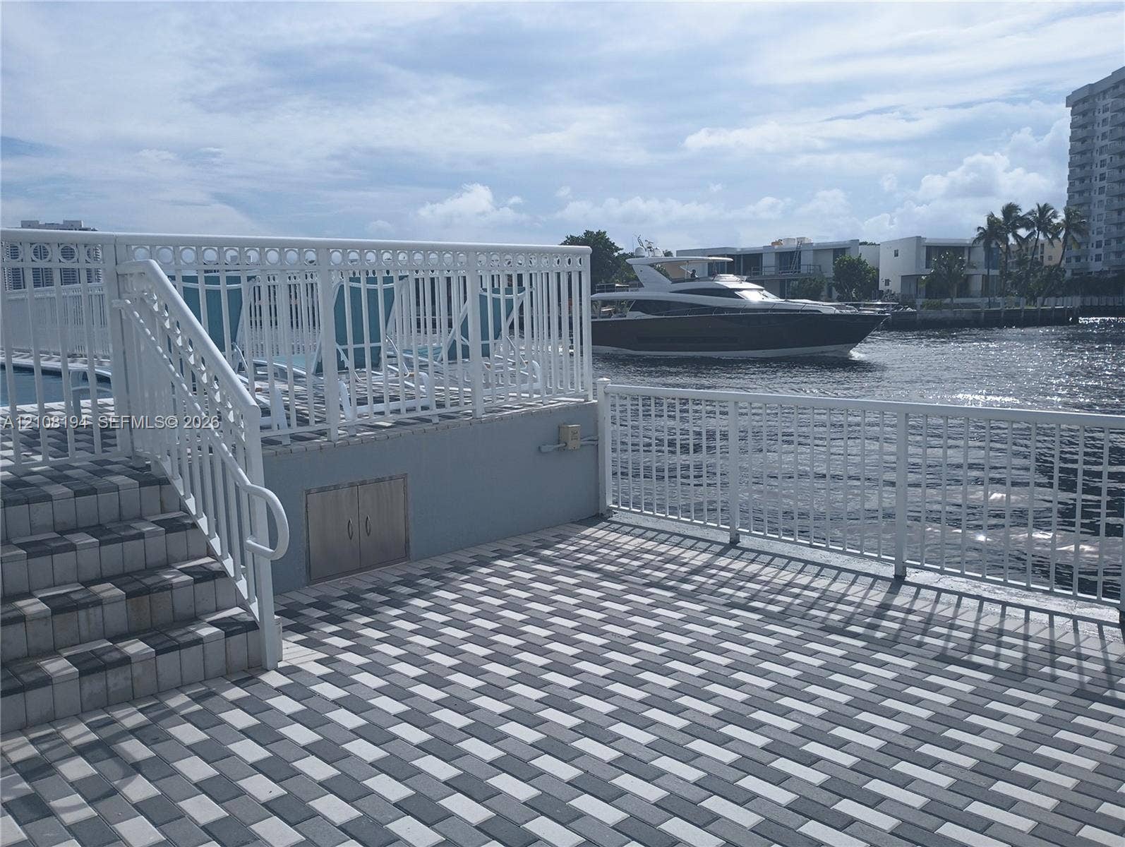 Waterfront terrace featuring multi-tone paved surfacing, white aluminum railings, built-in storage cabinet, and elevated staircase