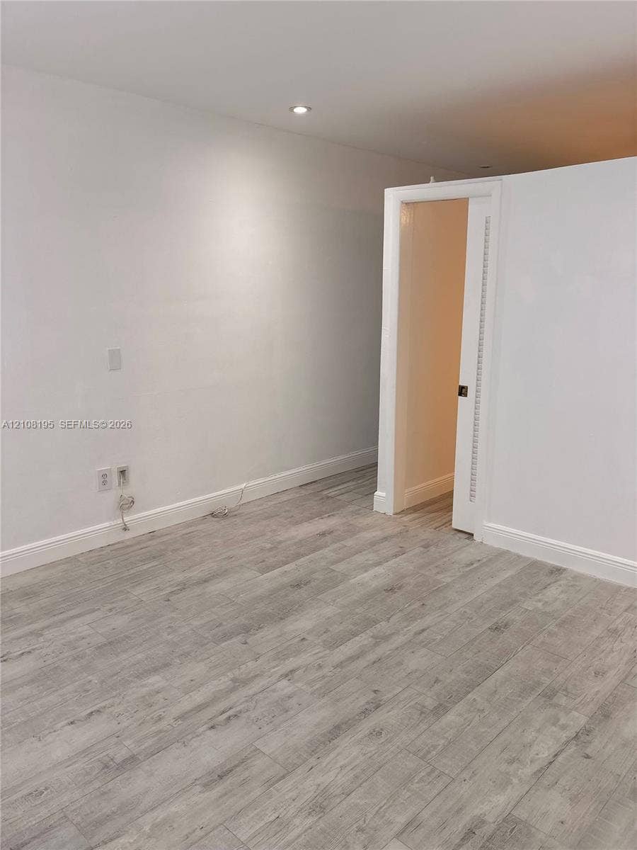 Interior space featuring wood-finish flooring, recessed ceiling lighting, and a white interior door with a louvered panel