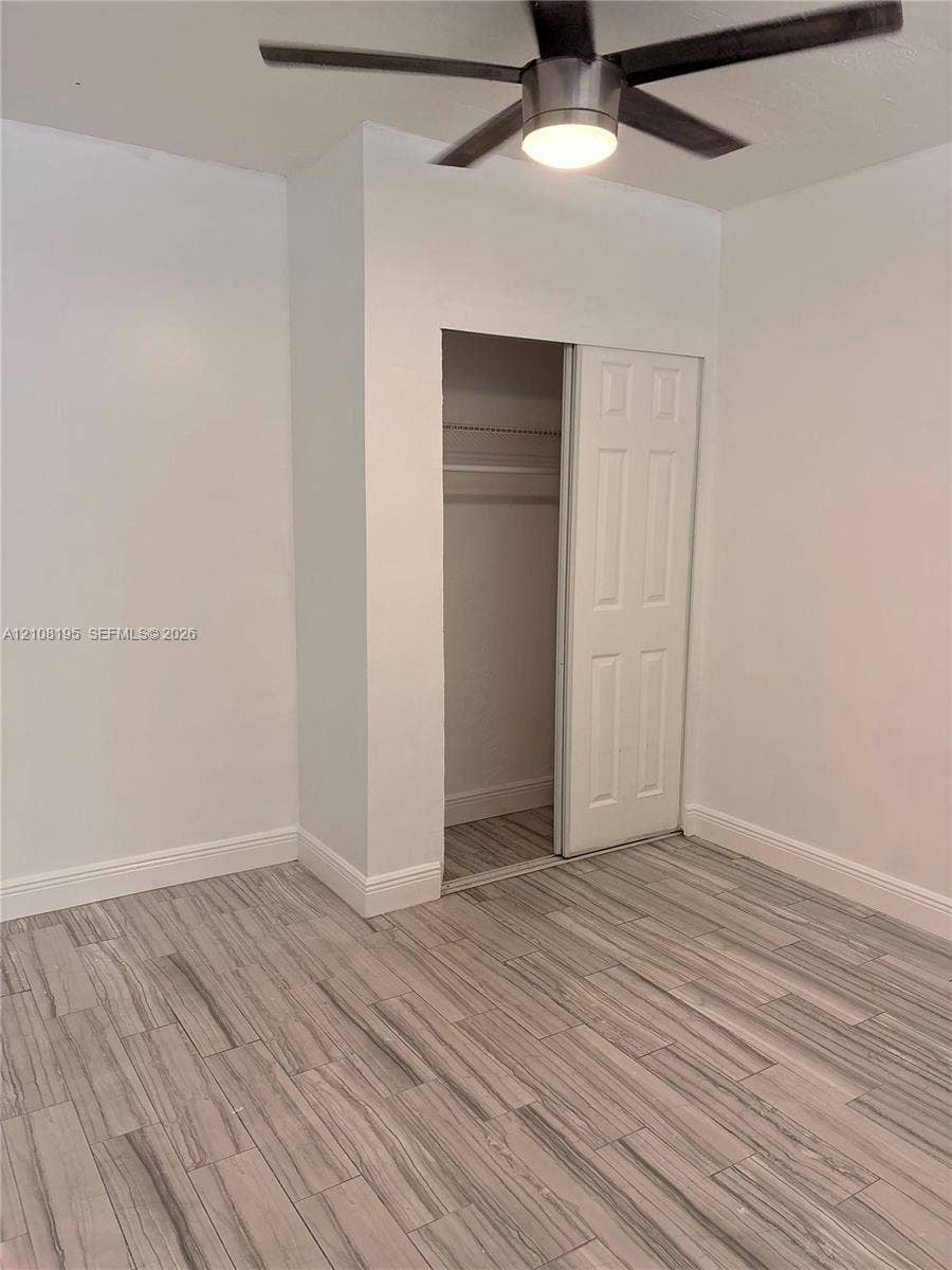 Room featuring wood-finish tile flooring, a neutral color palette, a ceiling fan with integrated lighting, and a closet with a paneled sliding door
