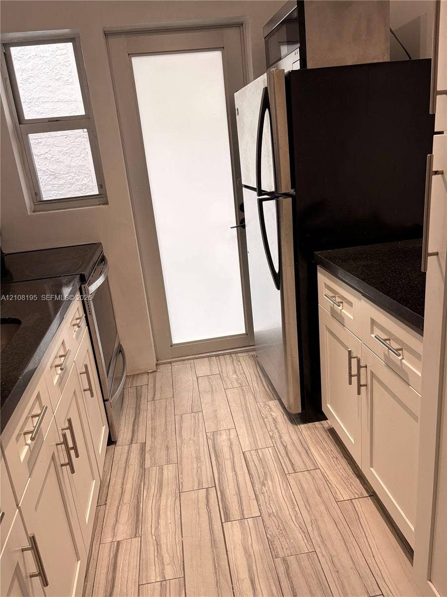 Kitchen featuring white shaker-style cabinetry, dark stone countertops, wood-finish tile flooring, a glass-panel exterior door, and stainless steel appliances