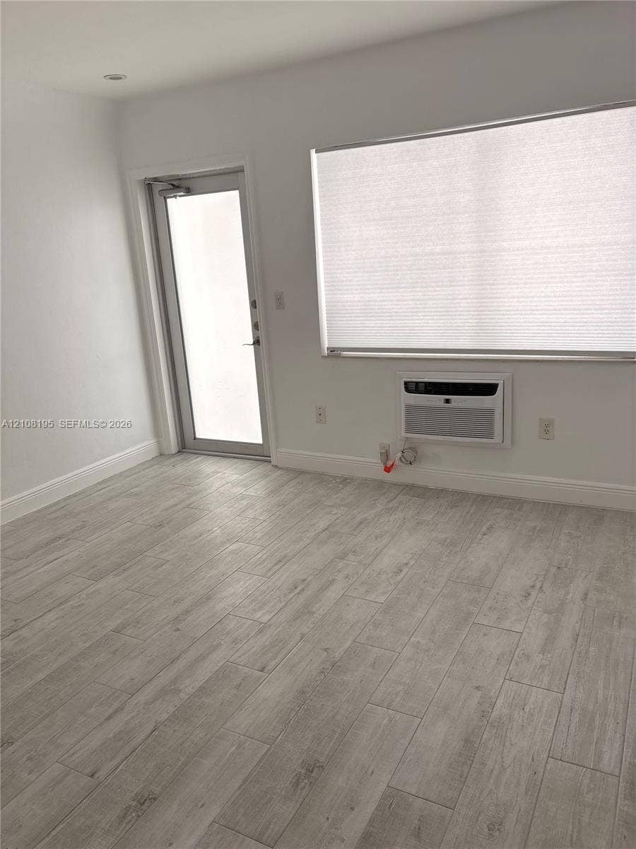 Wood-finish flooring, recessed ceiling lighting, large window with pleated shade, and wall-mounted air conditioning unit