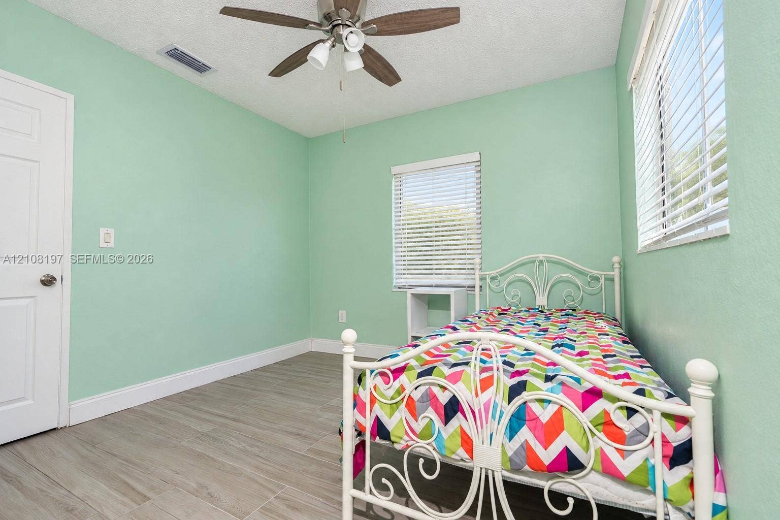 Wood-finish tile flooring, ceiling fan with integrated lighting, and dual windows equipped with horizontal blinds
