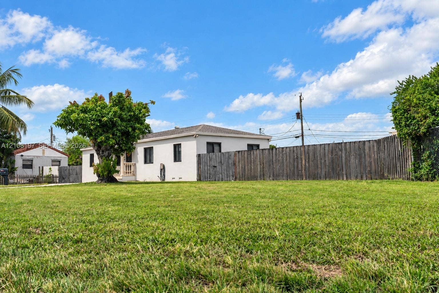 Expansive lawn with mature landscaping, enclosed by a wood privacy fence and featuring a stucco-finish exterior