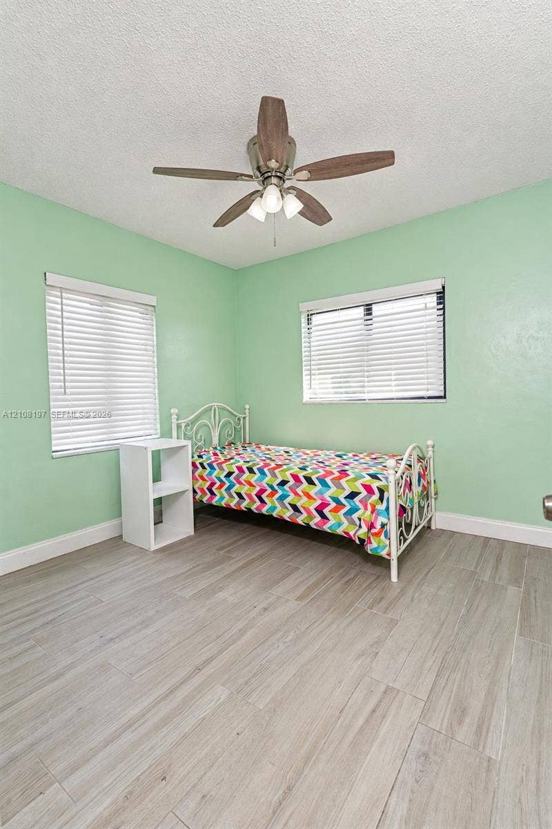 Room featuring wood-finish tile flooring, two windows with horizontal blinds, and a ceiling fan with integrated light fixture