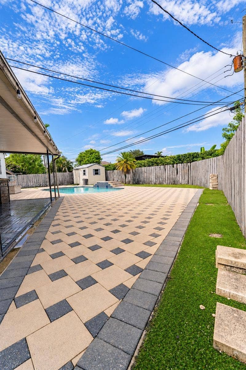 Expansive backyard featuring a custom paver patio, in-ground swimming pool, perimeter wood fencing, artificial turf, and a detached storage structure