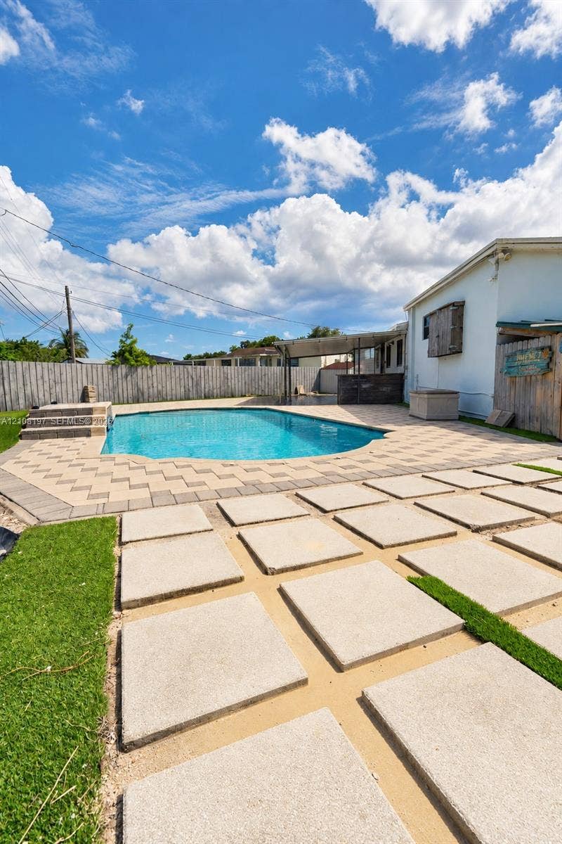 In-ground swimming pool with stone paver decking, decorative concrete stepping stones, synthetic grass, and wood privacy fencing
