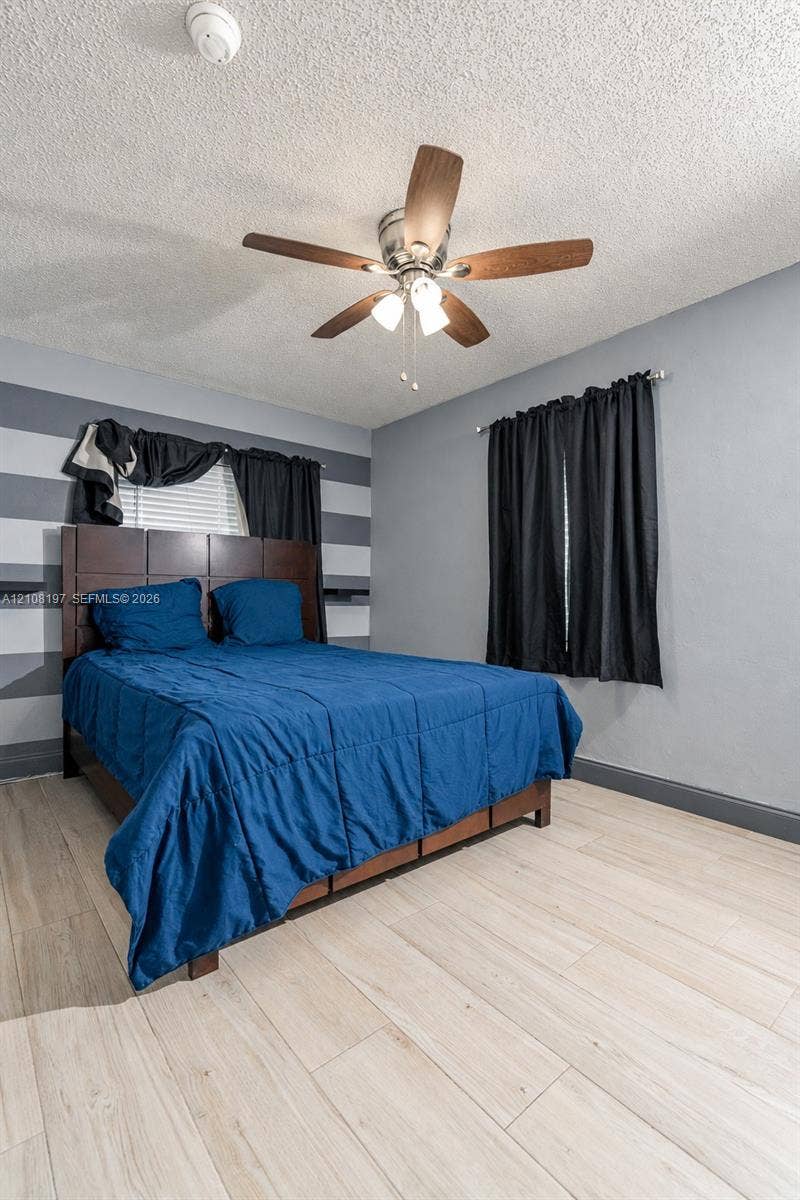 Bedroom featuring wood-finish flooring, a central multi-blade ceiling fan with integrated light fixture, and horizontal accent wall detailing