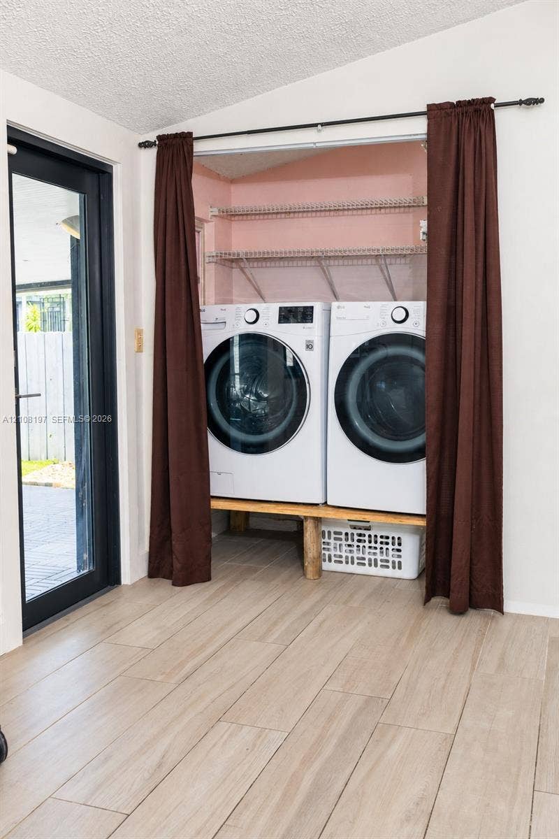 Laundry area featuring wood-finish tile flooring, a custom wood platform for laundry appliances, metal wire shelving, and a full-light glass door with a dark frame