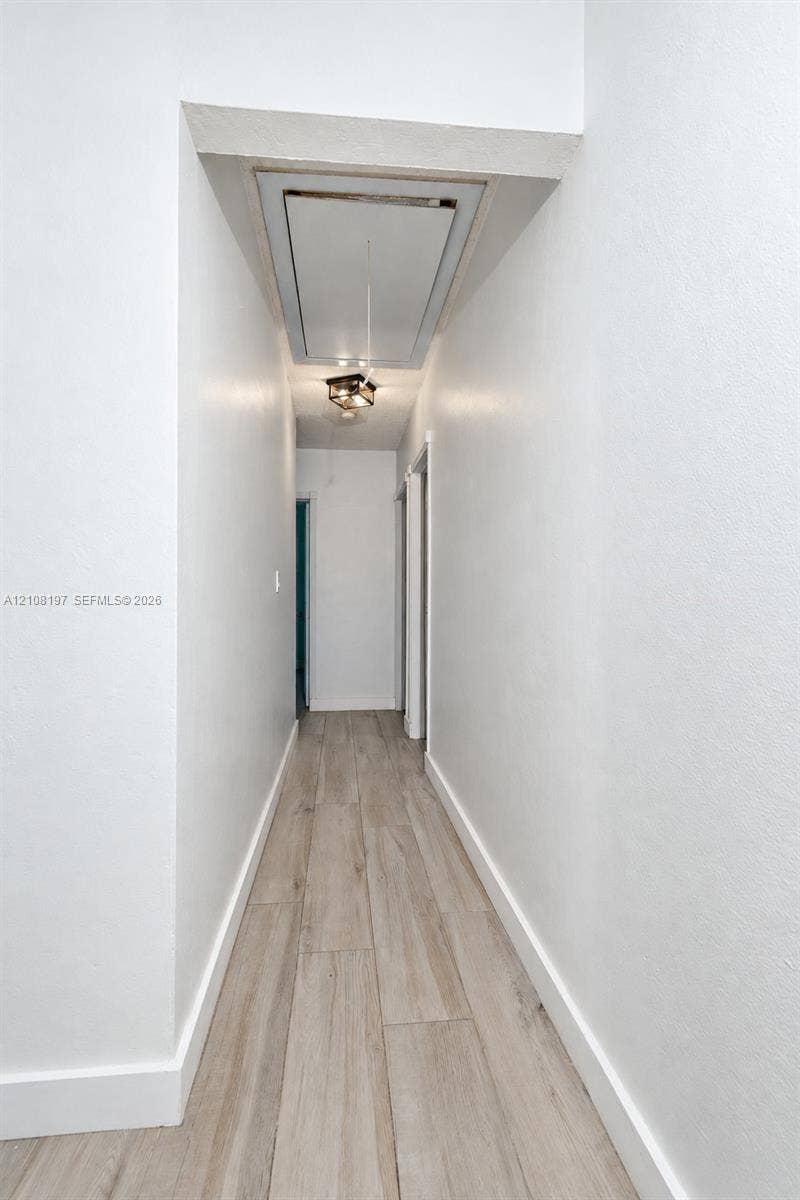Hallway featuring wood-finish flooring, smooth-finish walls, and a recessed ceiling access panel with an integrated light fixture