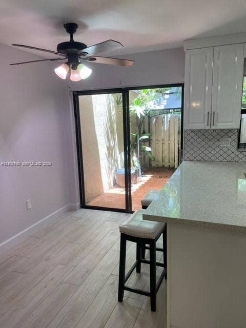 Kitchen featuring white shaker-style cabinetry, a quartz countertop, diamond-patterned tile backsplash, wood-finish flooring, and a sliding glass door