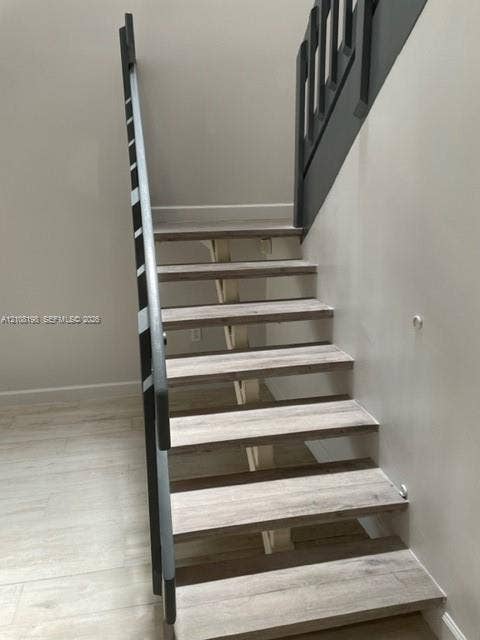Open-riser staircase featuring wood-finish treads, a structural central support, and contrasting dark-toned railings