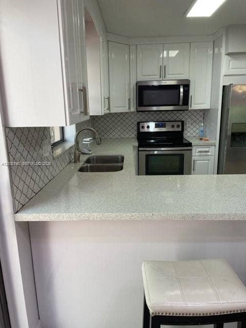 Kitchen featuring white cabinetry, solid-surface countertops, stainless steel appliances, and a patterned tile backsplash
