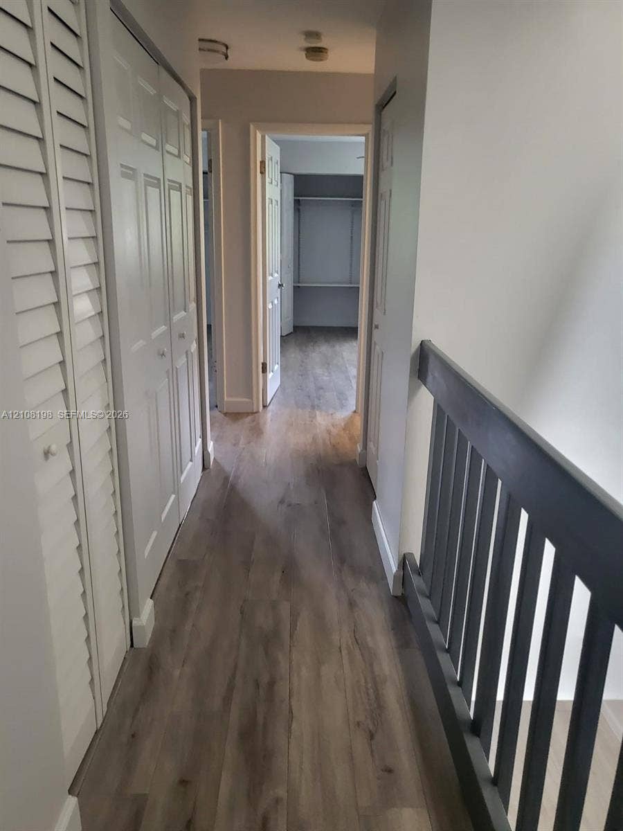 Hallway featuring wood-finish flooring, white louvered bi-fold closet doors, and a dark-toned vertical slat railing