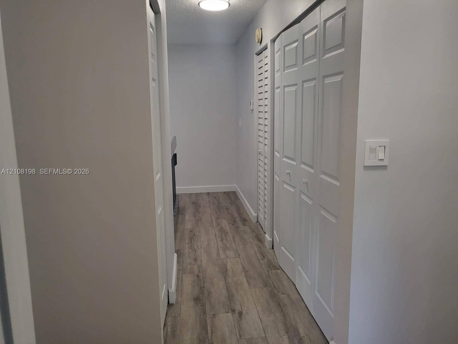 Hallway featuring wood-finish flooring, two sets of white paneled bifold closet doors, and flush-mount overhead lighting