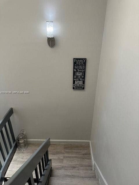 Staircase featuring wood-finish flooring, a metal-railed banister, and a brushed-nickel wall-mounted light fixture with a textured glass shade