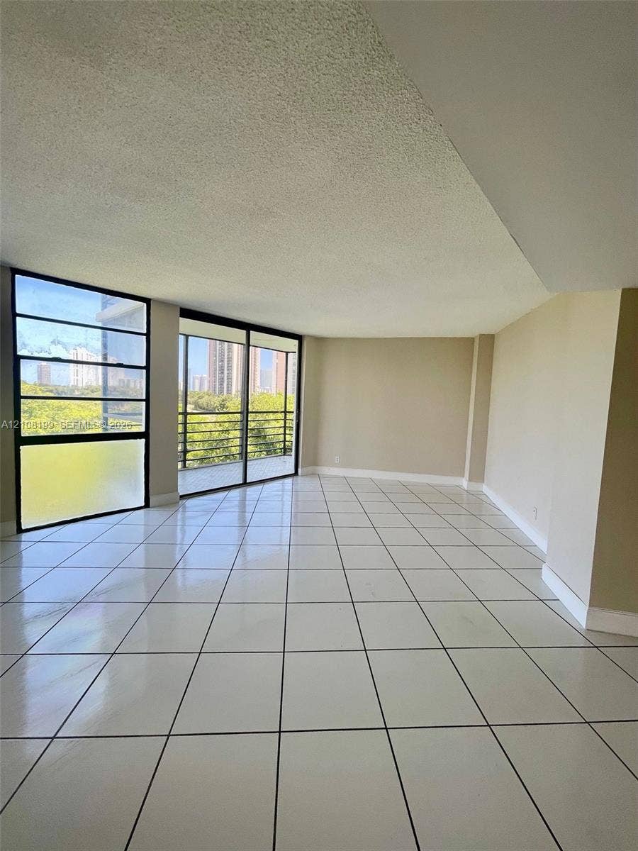20400 W Country Club Drive, #608, Aventura, Aventura, FL 33180 Interior space featuring large-format tile flooring, expansive floor-to-ceiling windows, sliding glass door access to a balcony, and textured ceiling finish