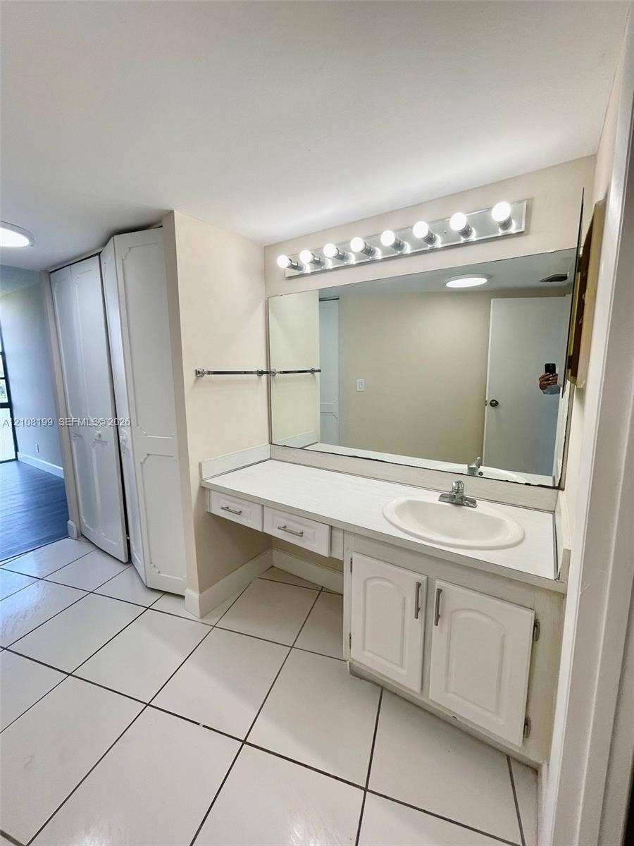 20400 W Country Club Drive, #608, Aventura, Aventura, FL 33180 Vanity with white cabinetry, integrated countertop and sink, large rectangular mirror, overhead vanity lighting, and ceramic tile flooring
