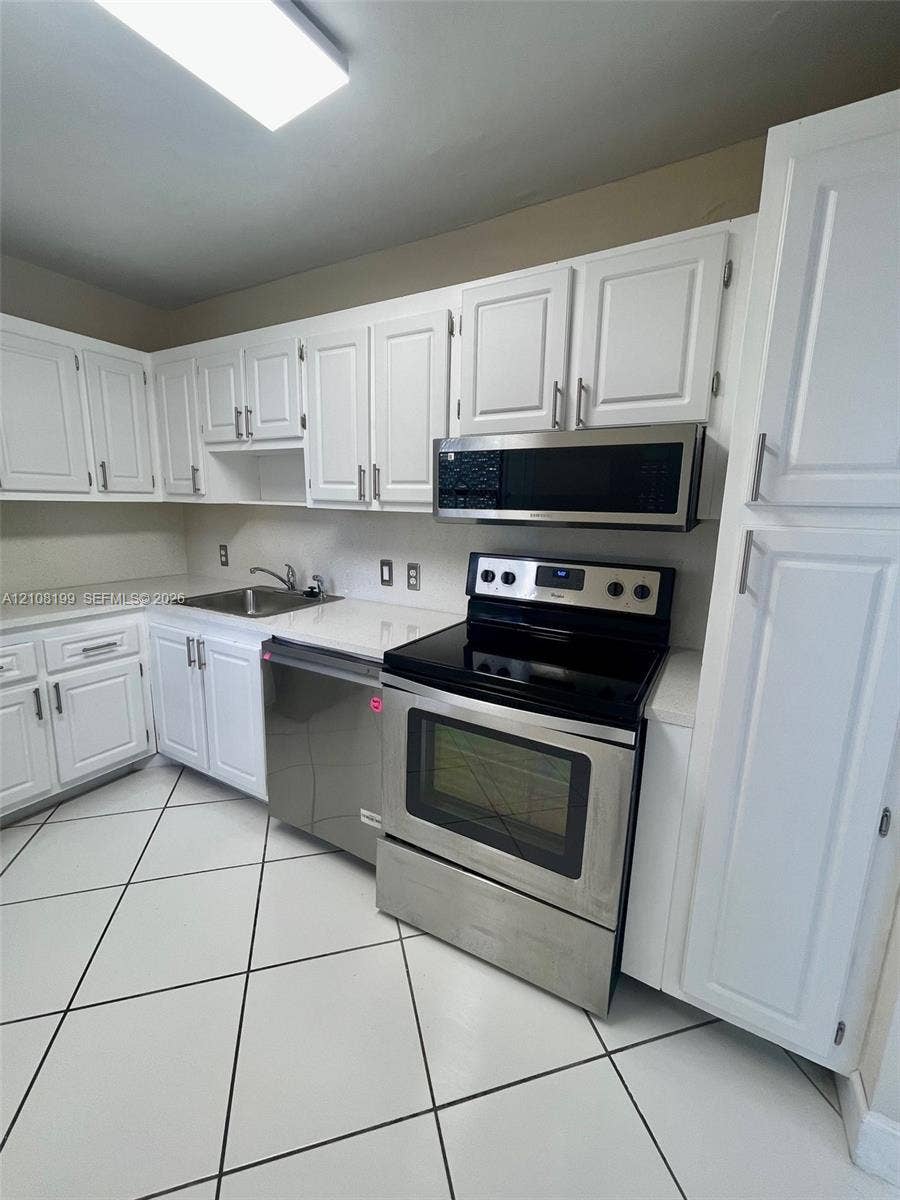 20400 W Country Club Drive, #608, Aventura, Aventura, FL 33180 Kitchen featuring white cabinetry, stainless steel appliances, solid-surface countertops, dual-basin stainless steel sink, and large-format tile flooring