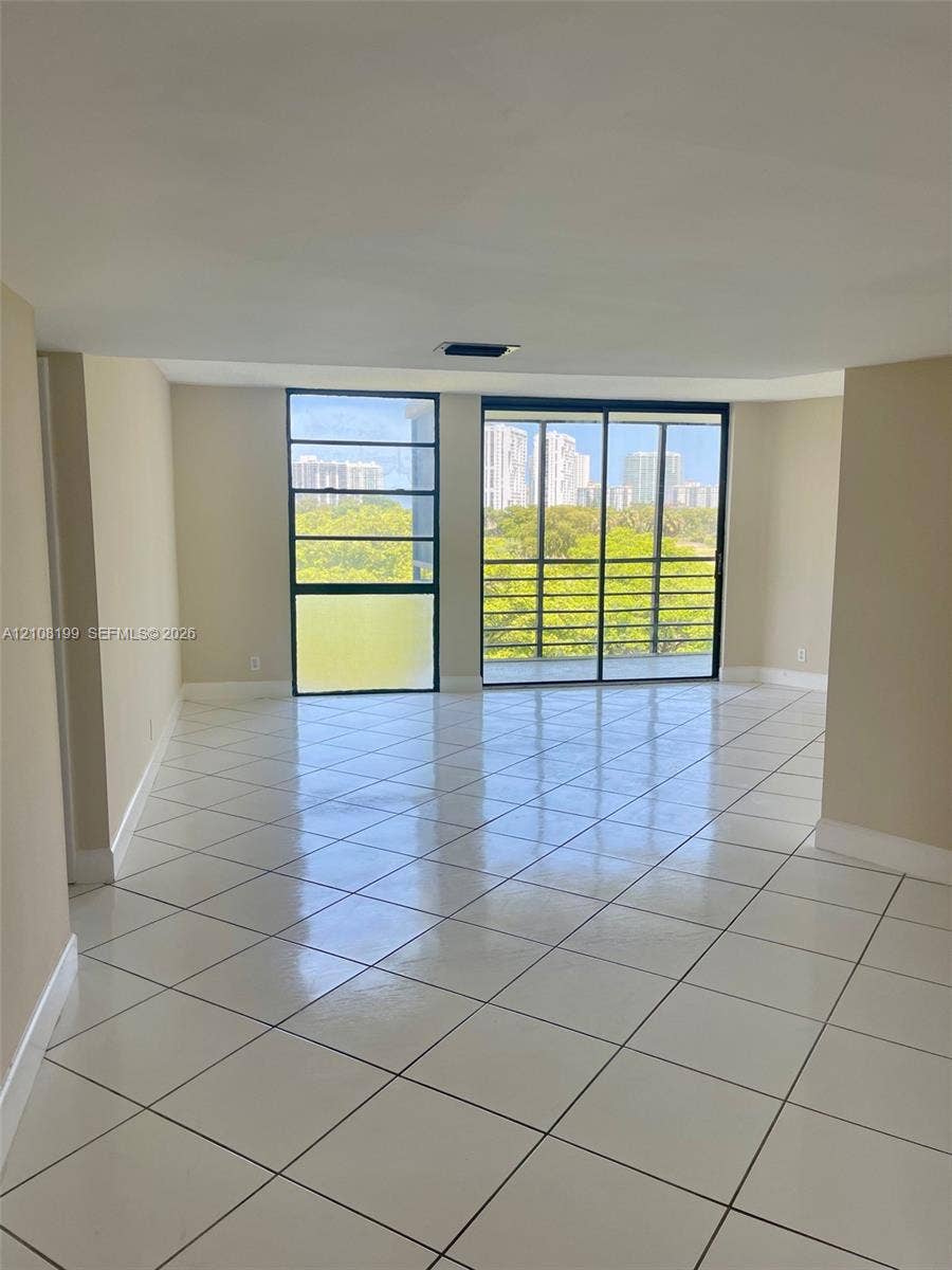 20400 W Country Club Drive, #608, Aventura, Aventura, FL 33180 Open-concept interior featuring large-format diagonal tile flooring, floor-to-ceiling windows, and sliding glass doors leading to a screened balcony