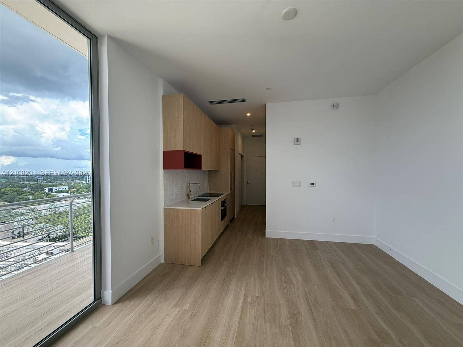 32 90 Ne 32 Street, #1115, Miami, Miami, FL 33127 Kitchenette featuring light-wood cabinetry, white stone countertops, built-in cooktop, and gold-finish hardware, paired with wood-finish flooring and a balcony with metal railing