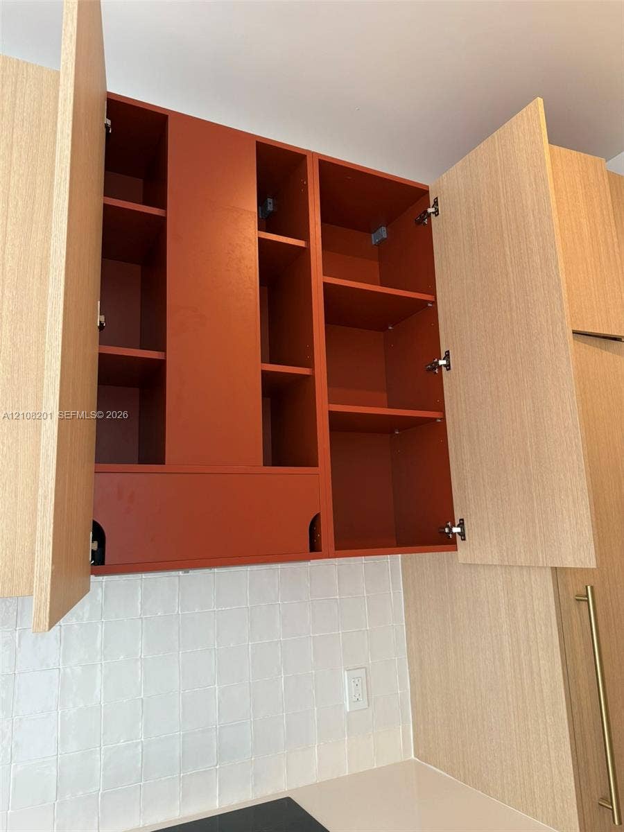 32 90 Ne 32 Street, #1115, Miami, Miami, FL 33127 Custom cabinetry featuring wood-finish doors, interior shelving with a matte-finish rust-tone backing, and square-profile white tile backsplash