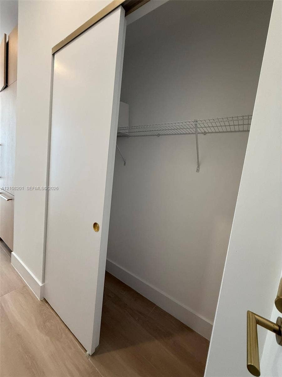 32 90 Ne 32 Street, #1115, Miami, Miami, FL 33127 Sliding door closet featuring a brass-tone hardware track, recessed circular brass pull, wood-finish flooring, and integrated wire shelving