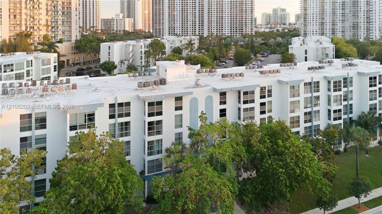 Mid-rise residential building featuring a white facade, multi-level structural design, uniform window grid, and integrated green space with mature trees