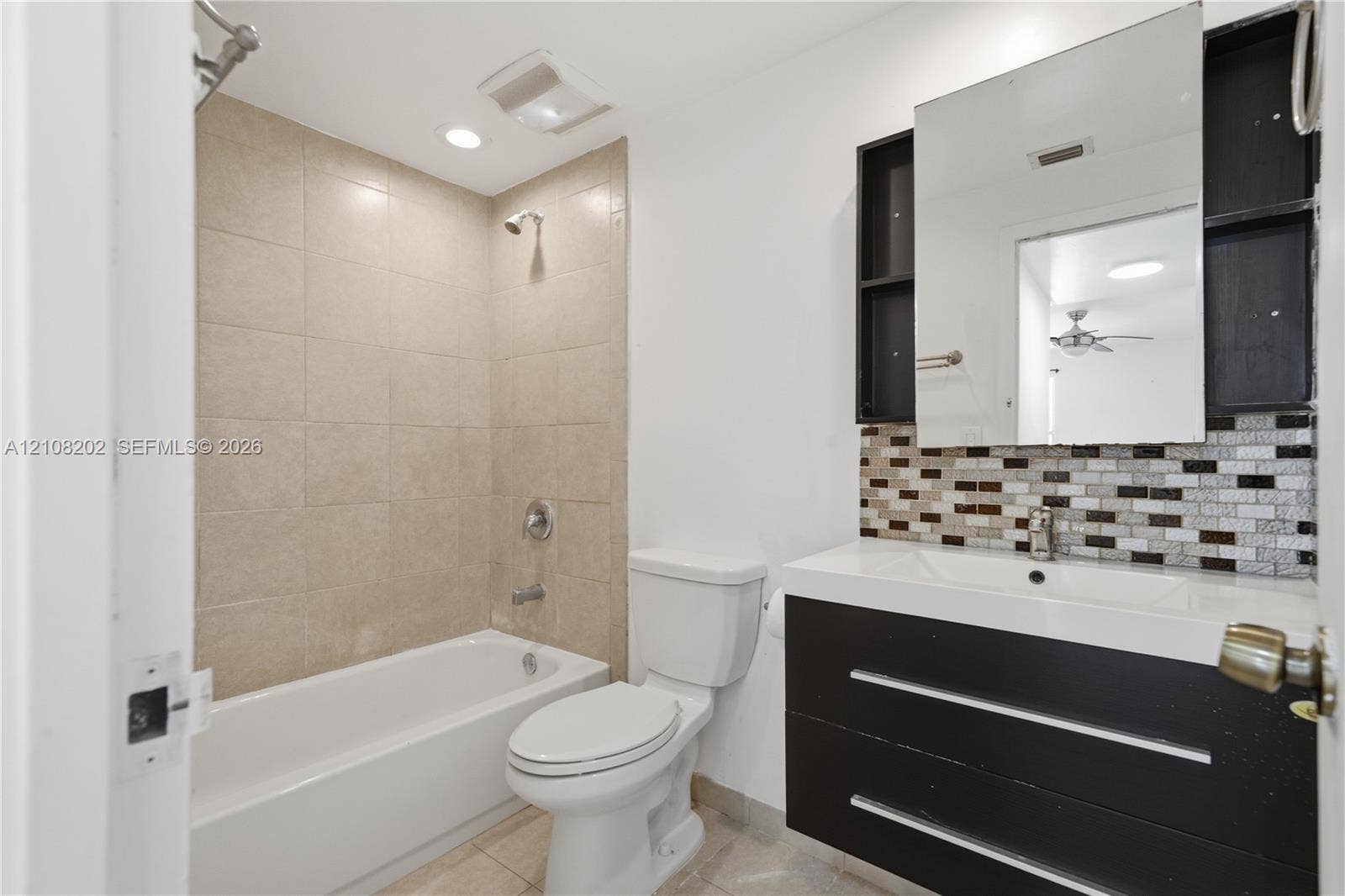 Bathroom featuring a floating dark-finish vanity with an integrated basin, multi-toned mosaic tile backsplash, medicine cabinet, and a bathtub with beige wall tiling