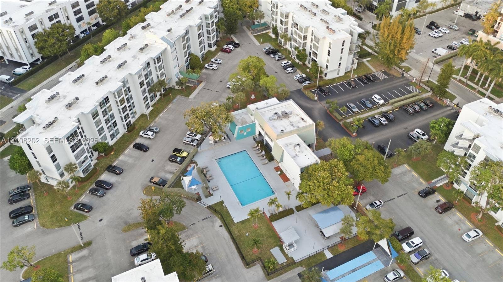 Aerial perspective featuring a communal swimming pool, paved surface parking areas, and mature landscaping