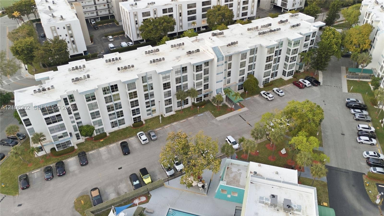Multi-story residential building featuring a flat roof, concrete exterior, dedicated surface parking, and manicured landscaping