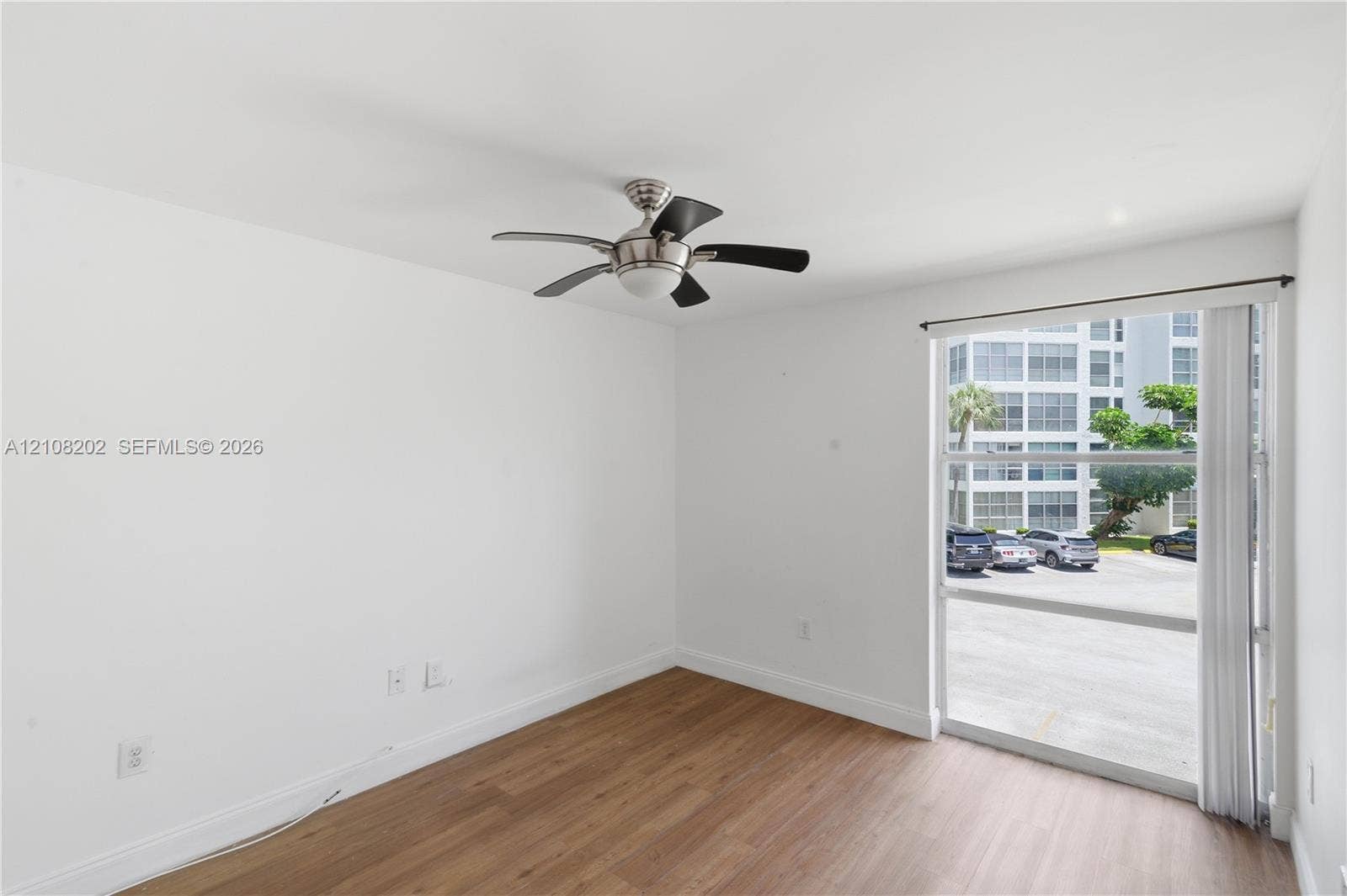 Wood-finish flooring, ceiling fan with integrated lighting, and floor-to-ceiling glass sliding door with vertical blinds