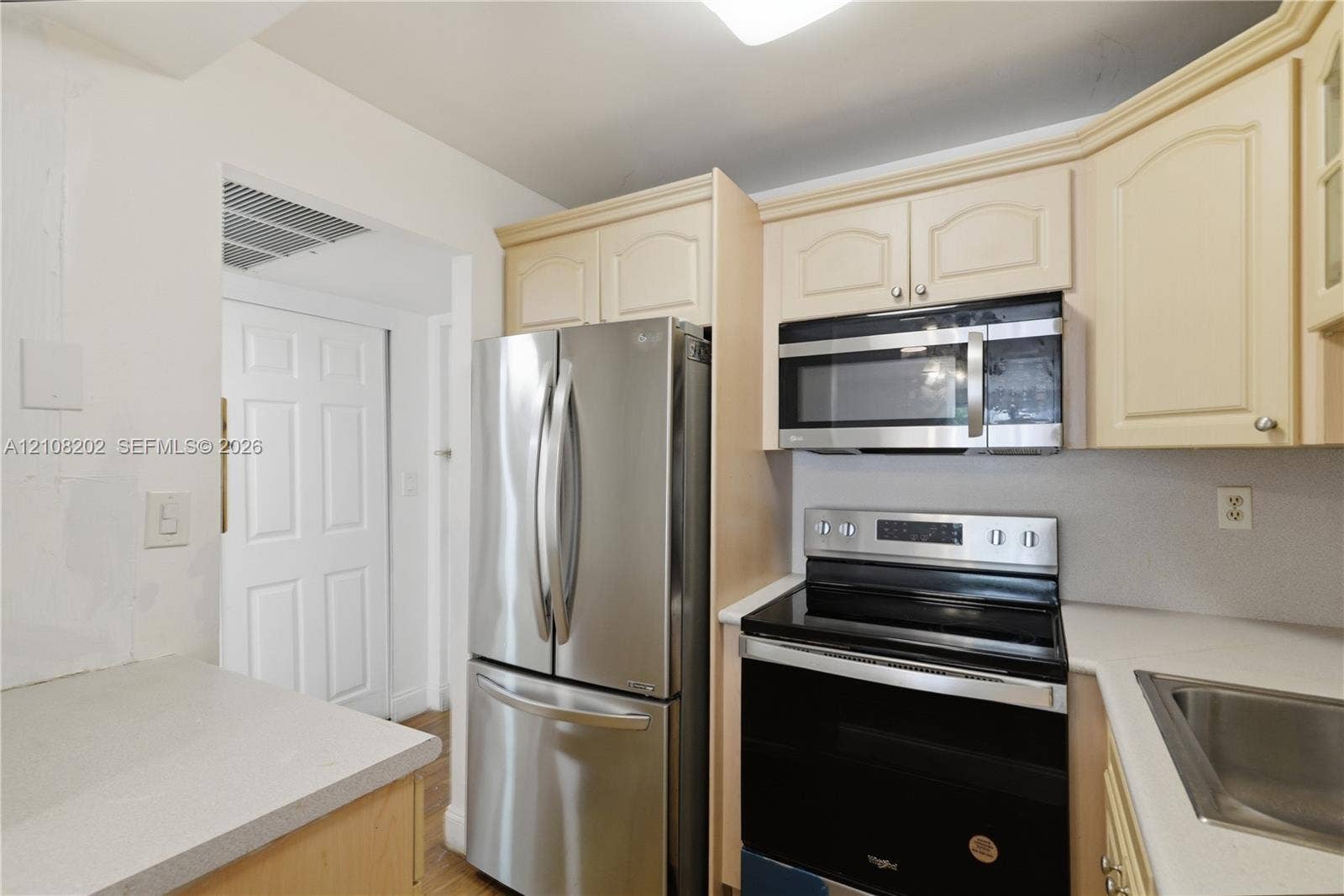 Kitchen featuring stainless steel French-door refrigerator, built-in microwave, electric range, solid-surface countertops, and light-tone cabinetry