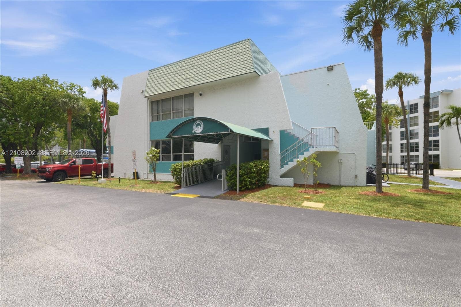 Two-story exterior featuring a textured stucco facade, a green arched awning, external metal staircase, and an asphalt parking area