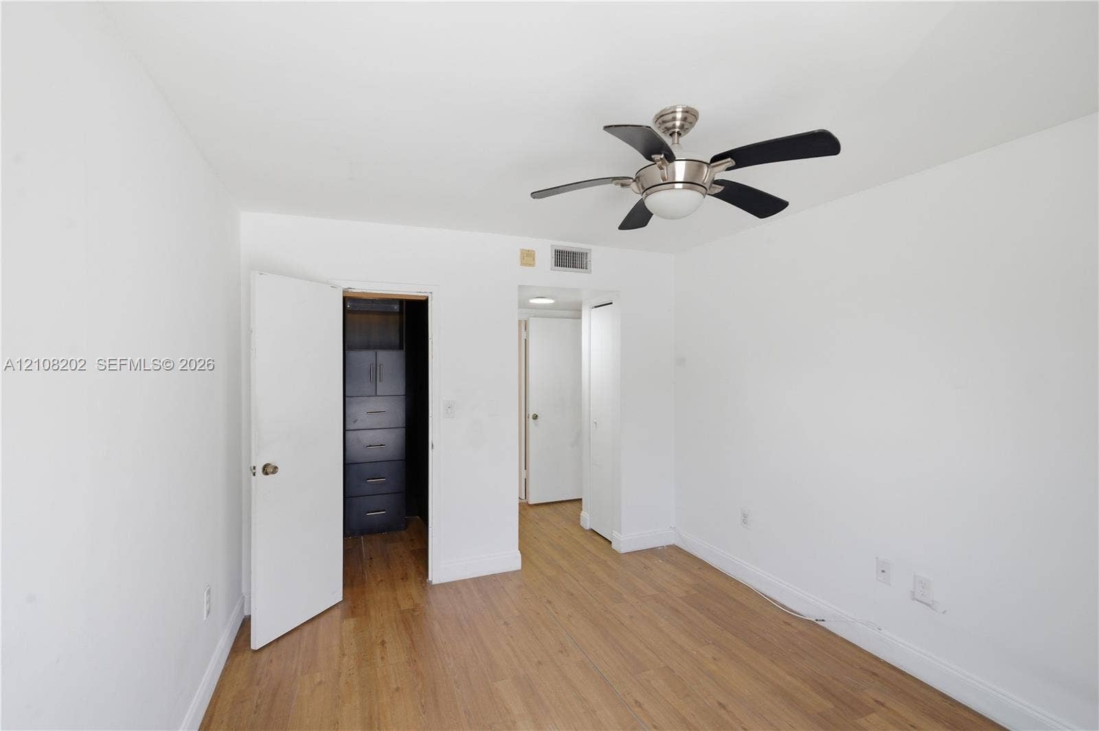 Room featuring wood-finish flooring, a multi-blade ceiling fan with integrated lighting, and built-in closet cabinetry