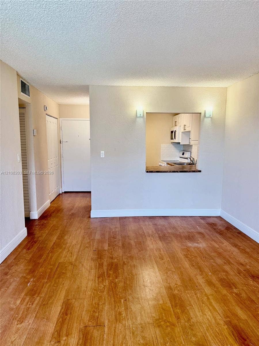 801 NW 47th Avenue, #619W, Miami, Miami, FL 33126 Wood-finish flooring throughout, wall-mounted light fixtures, and a pass-through opening with a solid-surface ledge