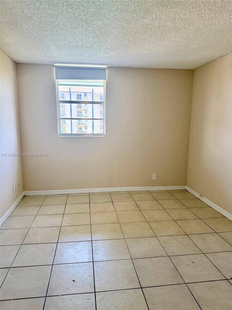 801 NW 47th Avenue, #619W, Miami, Miami, FL 33126 Interior space featuring neutral wall tones, large-format ceramic floor tiles, and a window with a roller shade