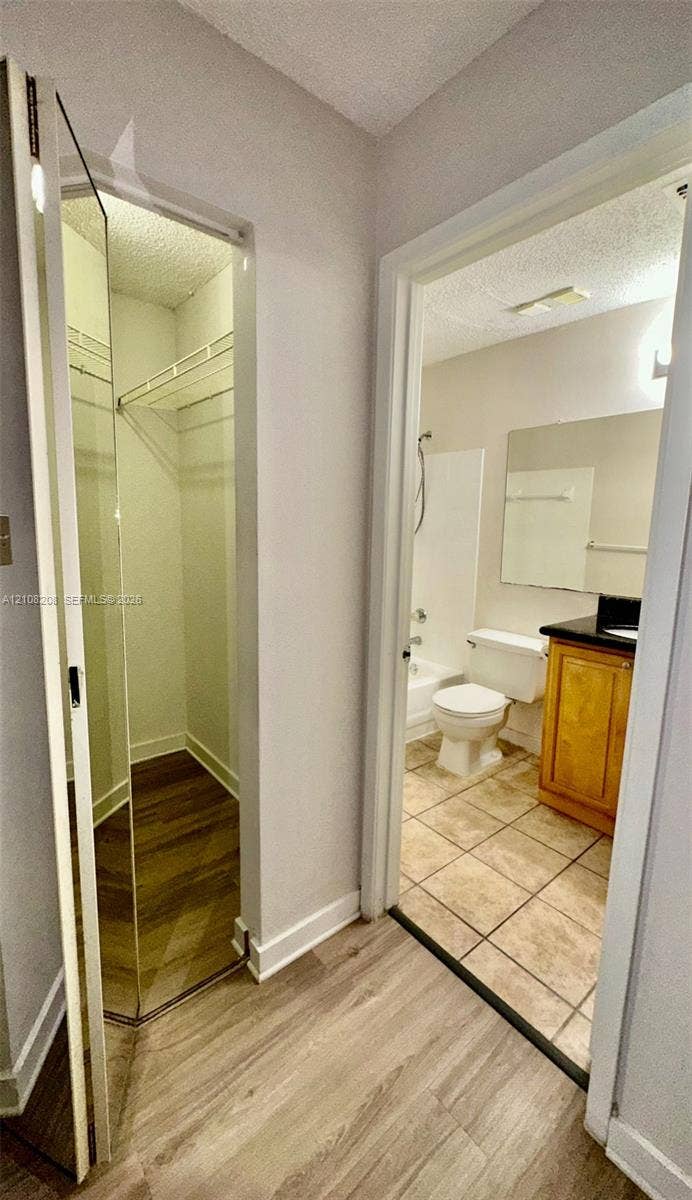 Coral Springs, Coral Springs, FL 33071 Walk-in closet with wire shelving and wood-finish flooring, featuring a bathroom with a wood-finish vanity cabinet, stone countertop, ceramic tile flooring, and a shower-tub combination