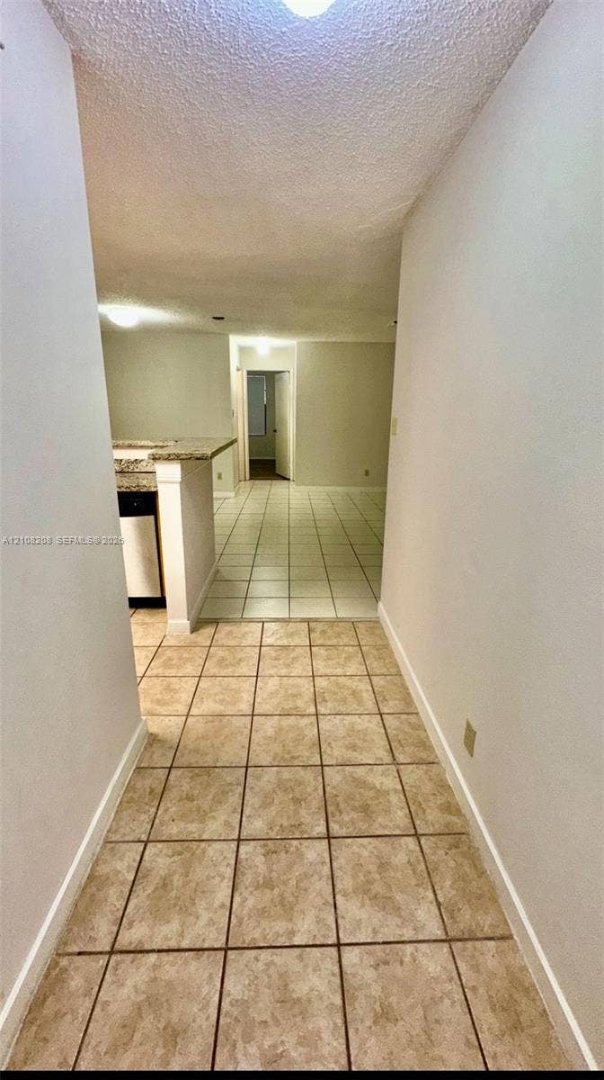 Coral Springs, Coral Springs, FL 33071 Interior hallway featuring tile flooring, neutral wall tones, and stone-surfaced counter peninsula