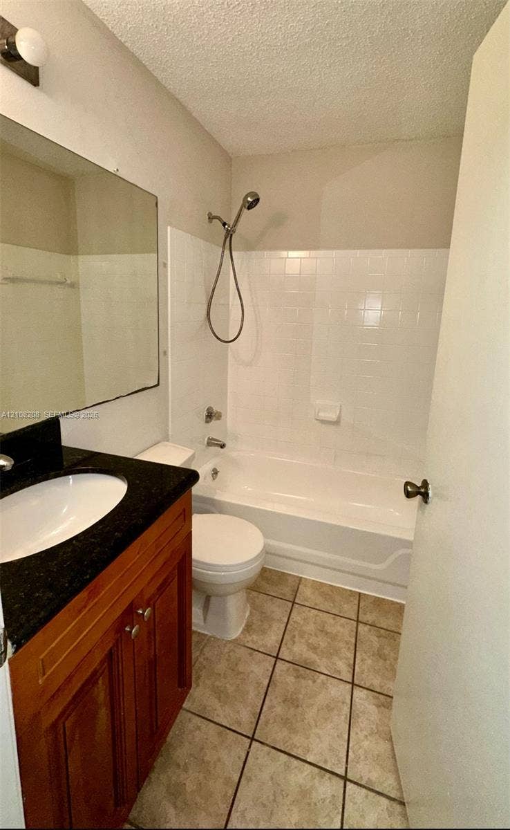 Coral Springs, Coral Springs, FL 33071 Bathroom featuring wood-finish cabinetry, a dark countertop with an integrated white sink, tile flooring, and a shower-tub combination with white wall tile