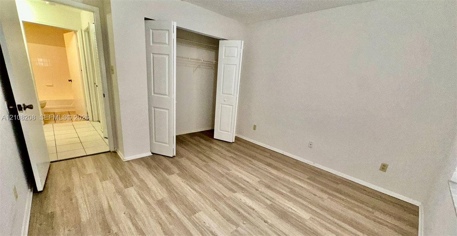 Coral Springs, Coral Springs, FL 33071 Room featuring wood-finish flooring, a bi-fold door closet with built-in shelving, and entry to a tiled space