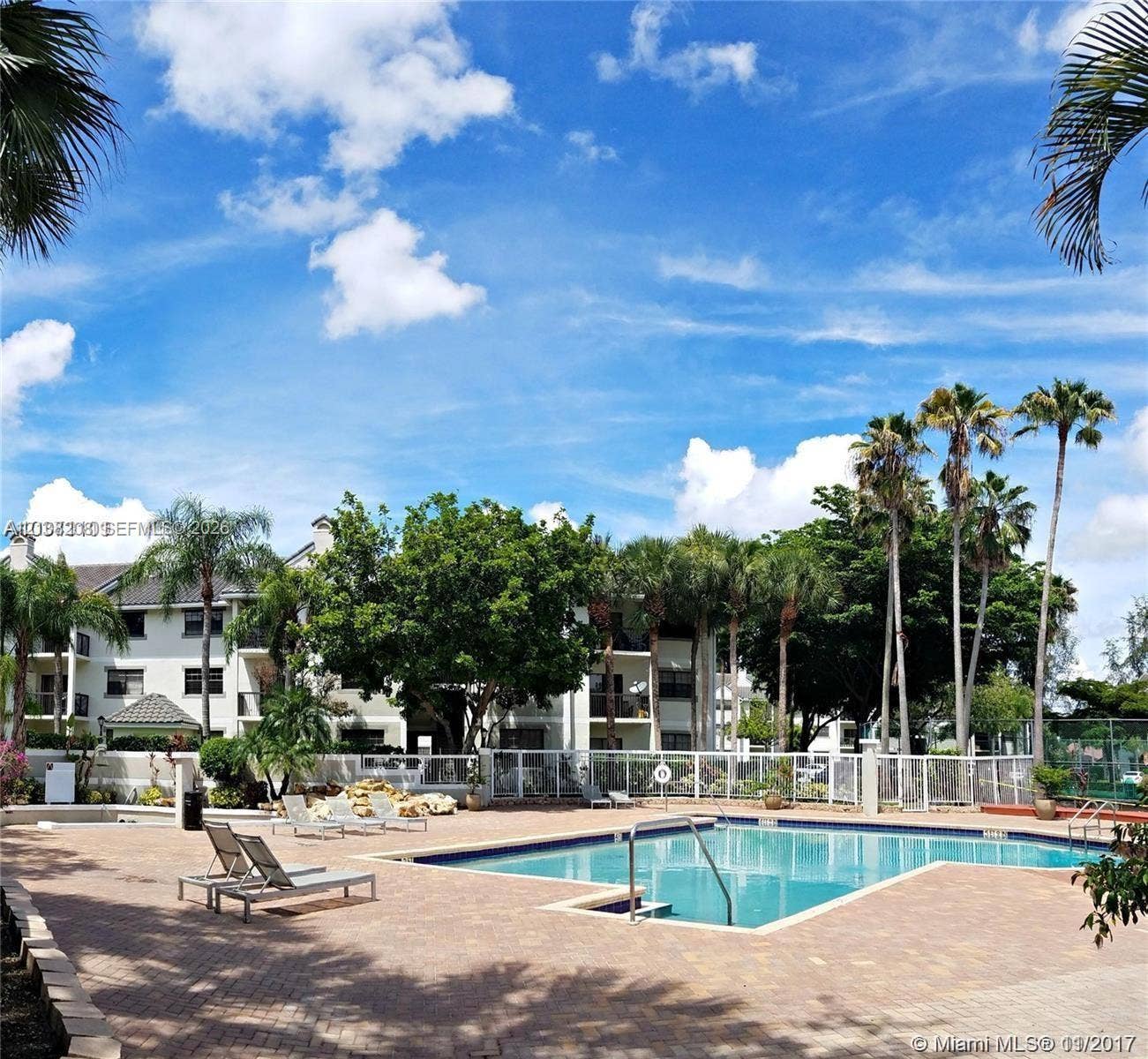 Coral Springs, Coral Springs, FL 33071 In-ground swimming pool with brick paver decking, surrounding perimeter fencing, and mature palm trees
