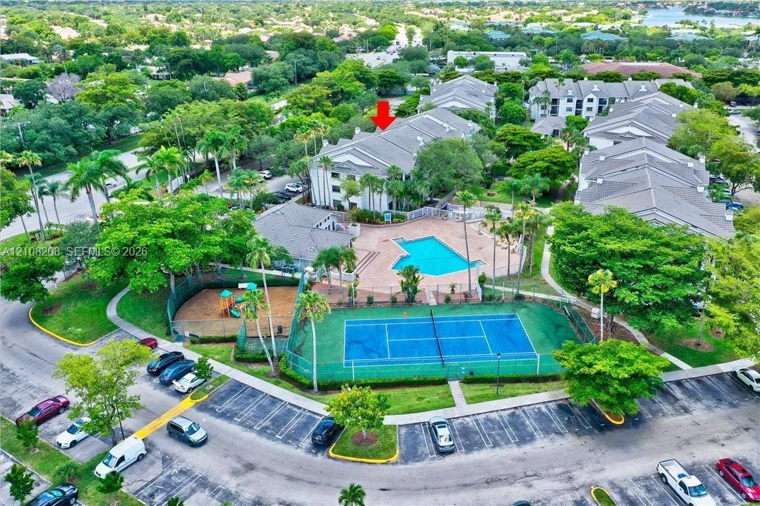 Coral Springs, Coral Springs, FL 33071 Multi-story building featuring a pitched roof, community swimming pool, fenced tennis court, and lush mature landscaping