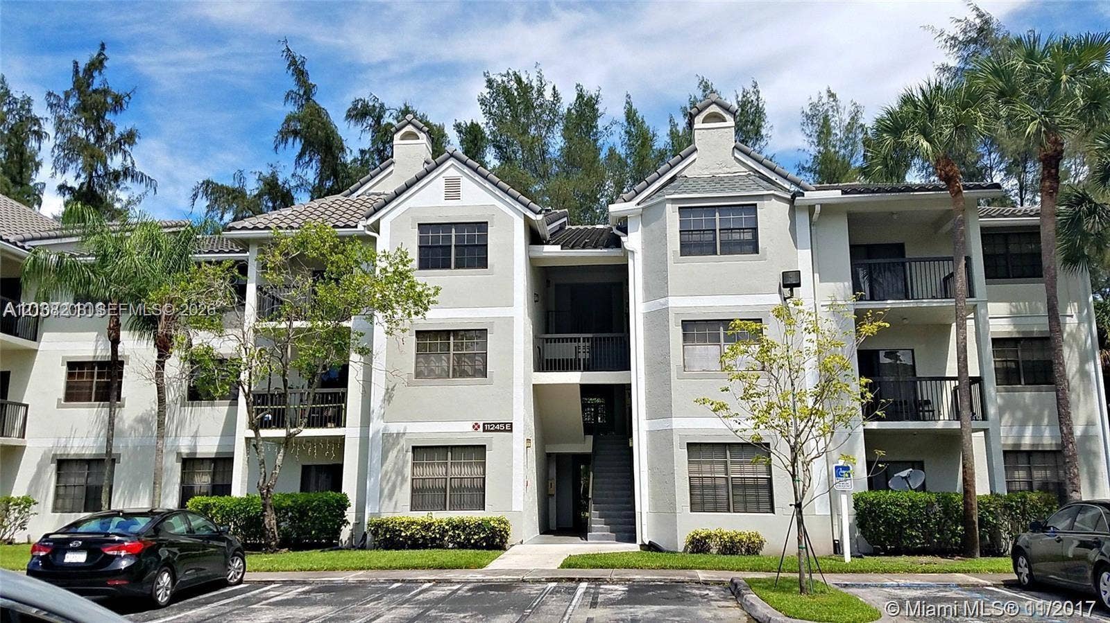 Coral Springs, Coral Springs, FL 33071 Multi-story stucco exterior featuring a pitched tile roof, private balconies with metal railings, and prominent gabled architectural accents