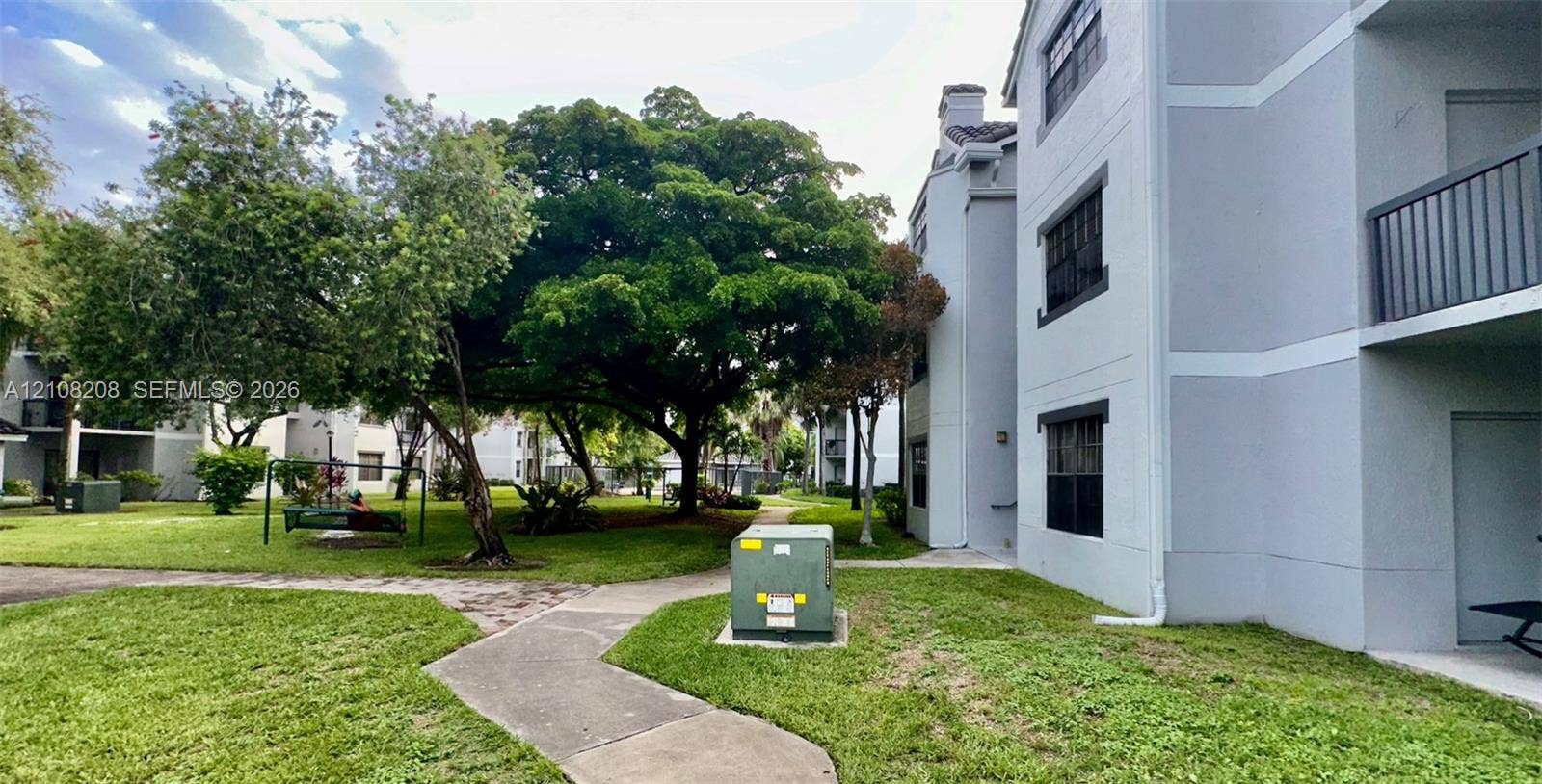 Coral Springs, Coral Springs, FL 33071 Multi-story exterior featuring a light gray facade, dark-framed windows, and private balconies, set among mature trees and manicured lawn areas with concrete pathways